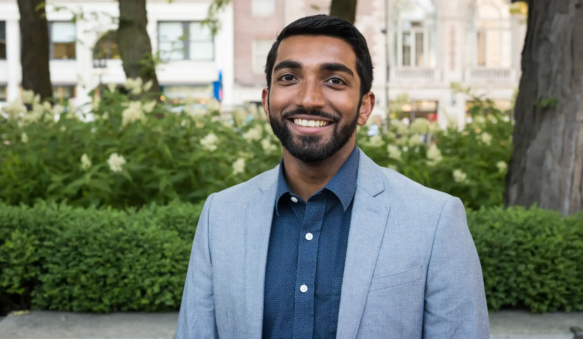 Headshot of Bejoy smiling in front of trees and foliage.